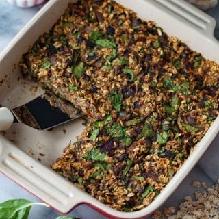 A red and white ceramic pan with baked savory oats, one piece is missing and there's a spatula in the pan