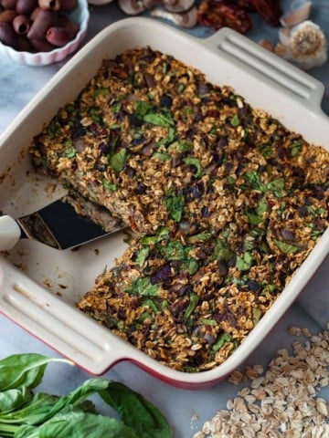 A red and white ceramic pan with baked savory oats, one piece is missing and there's a spatula in the pan