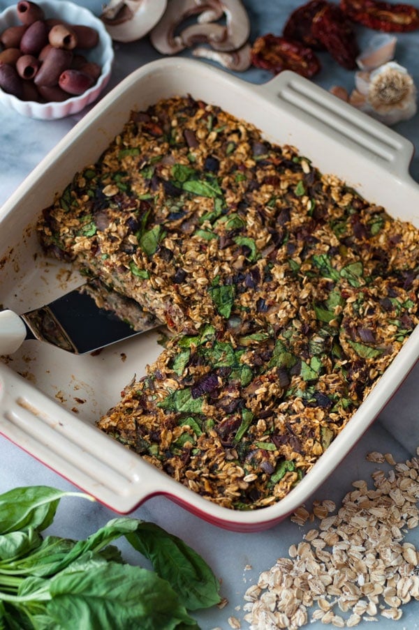 A red and white ceramic pan with baked savory oats, one piece is missing and there's a spatula in the pan