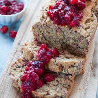 Sliced cranberry orange quick bread with a cranberry sauce on top, sitting on a wood board