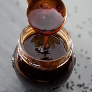 Healthy homemade vegan teriyaki sauce in a glass jar with a silver spoon dripping sauce into the jar
