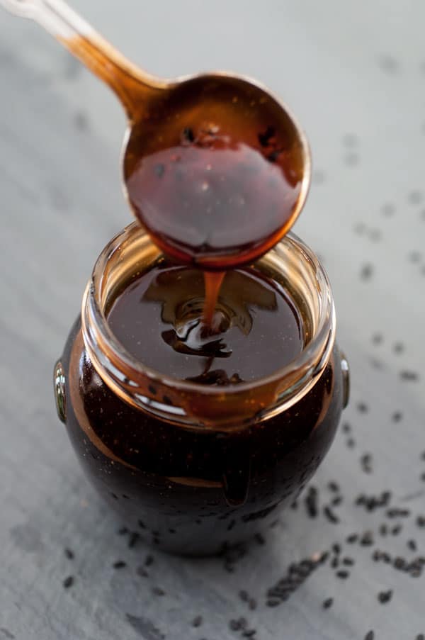 Healthy homemade vegan teriyaki sauce in a glass jar with a silver spoon dripping sauce into the jar