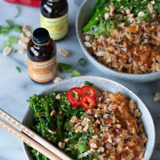 Vegan Ground Chik'n Bowls with chopsticks and another bowl behind it with bottles Nielsen-Massey Pure Orange and Lemon extract next to the bowls with peanuts, chopped green onion and a red pepper on a marble counter