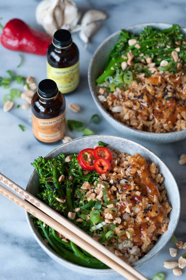 Vegan Ground Chik'n Bowls with chopsticks and another bowl behind it with bottles Nielsen-Massey Pure Orange and Lemon extract next to the bowls with peanuts, chopped green onion and a red pepper on a marble counter