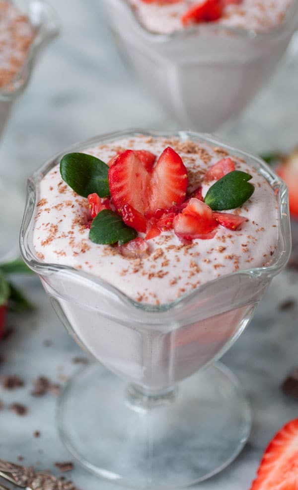 A close up shot of raw vegan strawberry mousse in a glass dish, garnished with chopped strawberries and green leaves