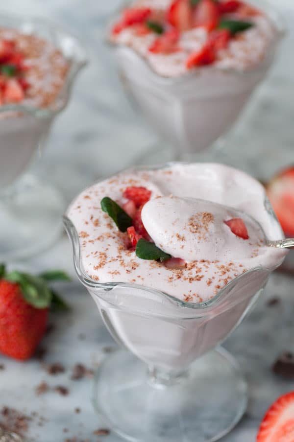 A glass dish of vegan strawberry mousse with a spoonful of mousse leaving the dish
