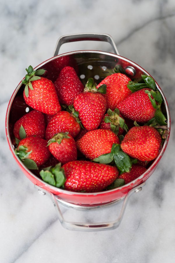 A red colander filled with fresh strawberries on a marble countertop