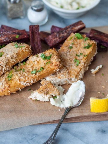 Vegan oven fried fish sticks with purple sweet potato fries and a spoon of tarter sauce and a lemon wedge.