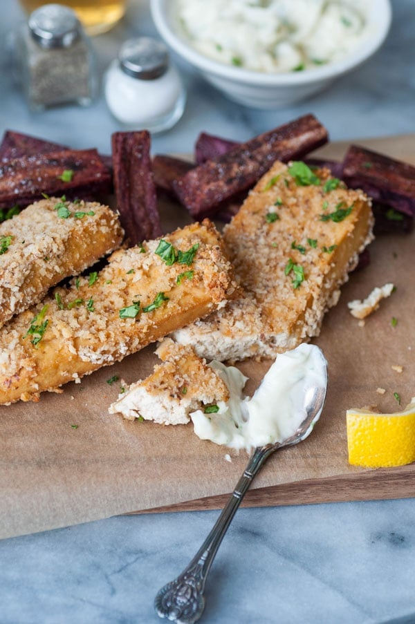 Vegan oven fried fish sticks with purple sweet potato fries and a spoon of tarter sauce and a lemon wedge.