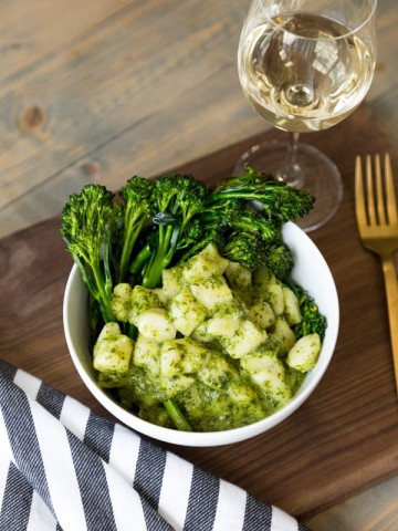 Pesto Gnocchi with Rapini a glass of wine, a gold fork, and a wood cutting board