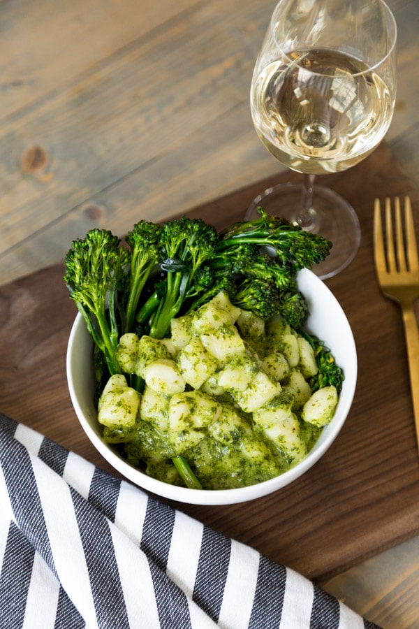Pesto Gnocchi with Rapini a glass of wine, a gold fork, and a wood cutting board