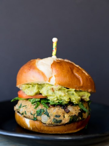 A spinach burger on a bun with avocado and tomato with a toothpick stuck in the center.