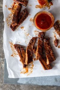 Slices of "Honey" BBQ BBQ ribz scattered on parchment paper with a dish of BBQ sauce in the upper right corner