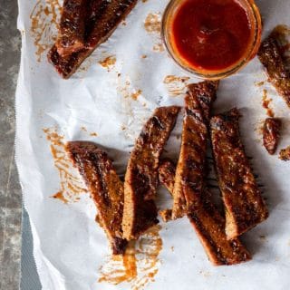 Pieces of "Honey" BBQ Ribz scattered on parchment paper with a dish of BBQ sauce in the upper right corner