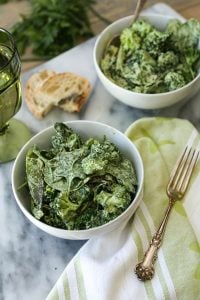 Two Green Goddess salads in white bowls with a green and white napkin and a silver fork on top and two pieces of bread on a marble surface