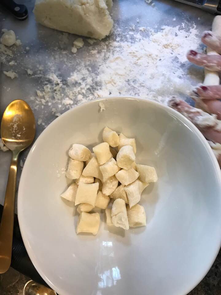 Sliced gnocchi in a white bowl on floured marble surface.