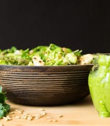 Green Spring Vegetable salad in a wood bowl on a wood surface with sunflower seeds sprinkled in front and part of a glass jar of creamy chimichurri sauce