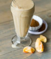 Peach Cobbler Smoothie with peaches and spices in the background on a wood cutting board.