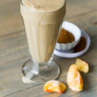 Peach Cobbler Smoothie with peaches and spices in the background on a wood cutting board.