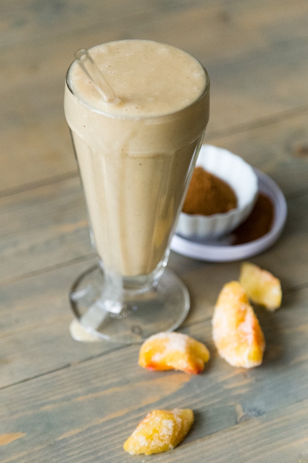 Peach Cobbler Smoothie with peaches and spices in the background on a wood cutting board. 