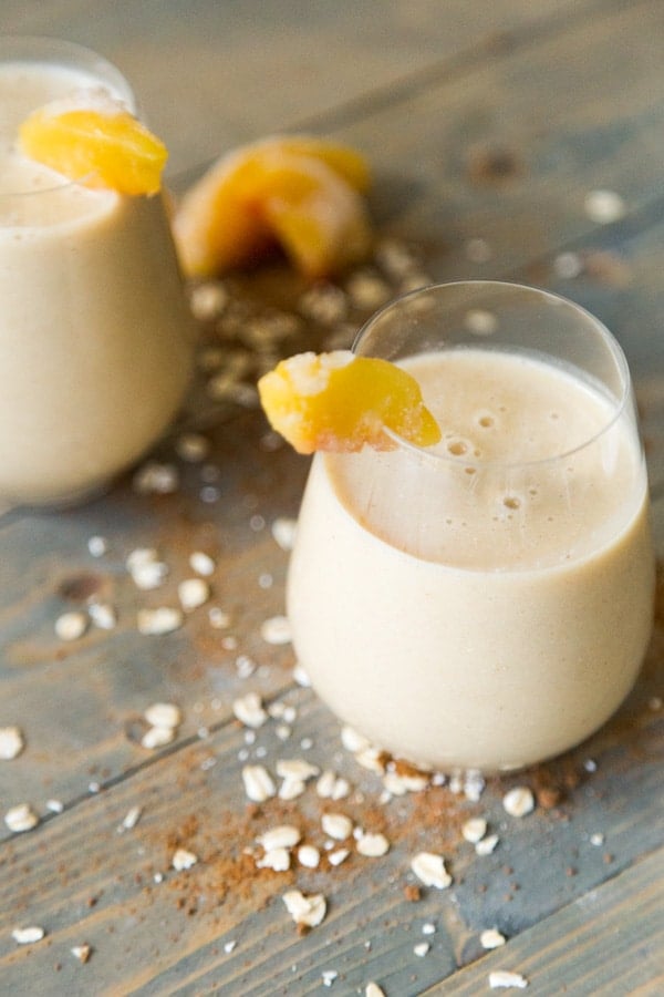 Peach Cobbler Smoothie with cinnamon, nutmeg, rolled oats, in wine glasses with peaches on the rim of the glass