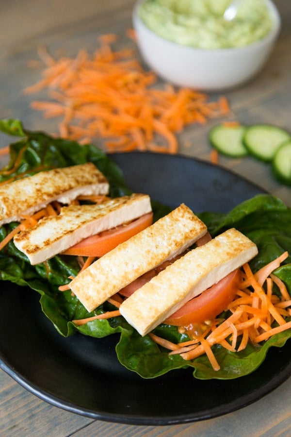 Tofu wrap on black plate with carrots, tomatoes, and cucumber