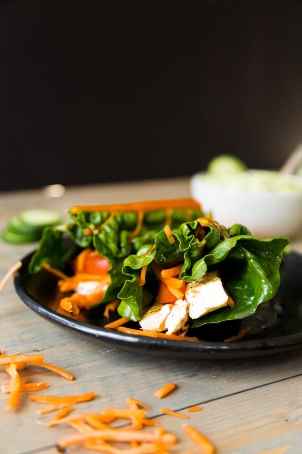 Tofu and vegetable wrap on a black plate with sauce in the background