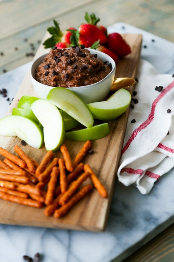 Brownie dessert hummus on board with pretzels, apples, and strawberries