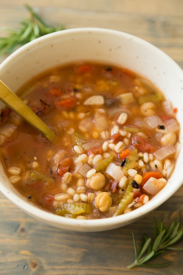 Italian Lemon Rosemary Barley Soup in a white bowl on a wood board with rosemary in the background