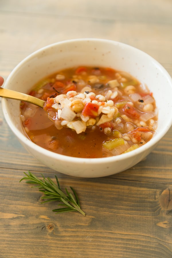 Italian Lemon Rosemary Barley Soup with a gold spoon on a wood cutting board with a piece of rosemary on top