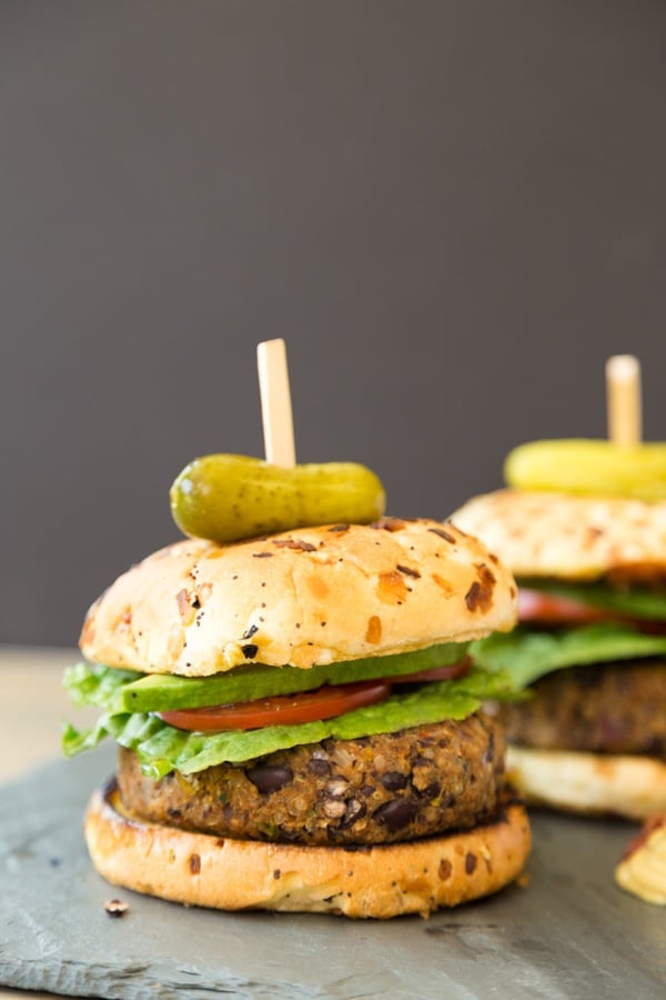 Two black bean burgers with onion buns and a pickle on top on a slate board