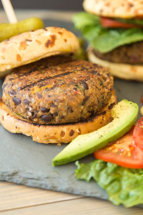 A spicy black bean burger on a bun with a piece of lettuce, slice of tomato and avocado slices on a slate board