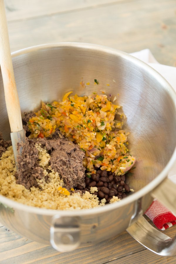 A steel bowl with ground black beans, sauteed vegetables, quinoa and spicey with a spatula in the bowl