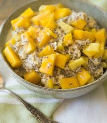 mango pineapple overnight oats in a grey bowl with a green napkin behind it and a silver spoon