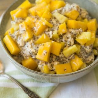 mango pineapple overnight oats in a grey bowl with a green napkin behind it and a silver spoon