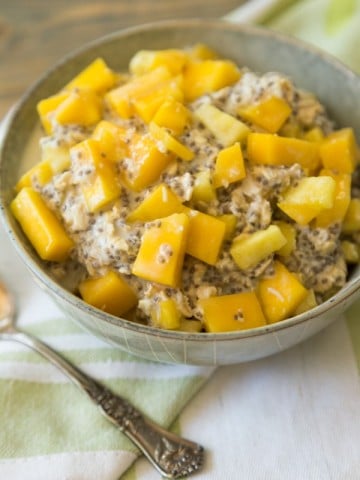 mango pineapple overnight oats in a grey bowl with a green napkin behind it and a silver spoon