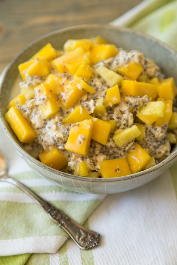 mango pineapple overnight oats in a grey bowl with a green napkin behind it and a silver spoon