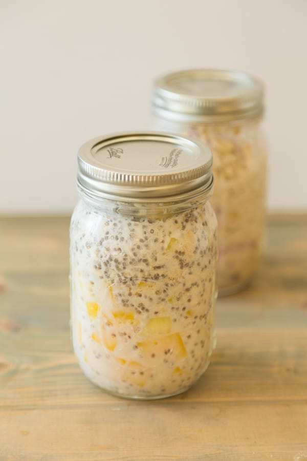 mango pineapple coconut overnight oats with chia seeds in a mason jar with another jar of overnight oats behind it