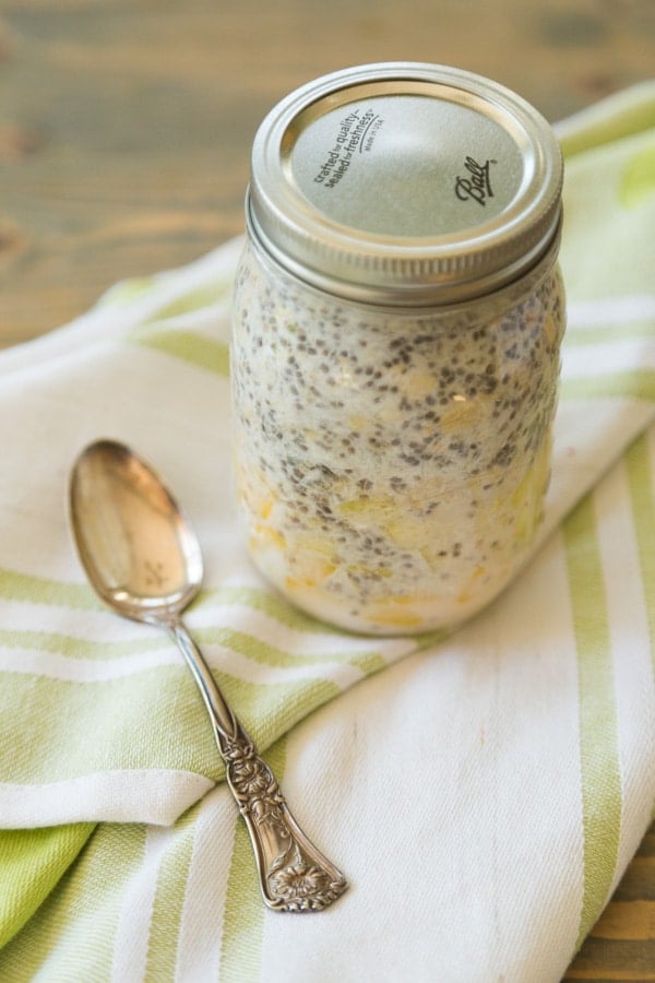 mango pineapple coconut overnight oats to go in a mason jar with a silver spoon next to it