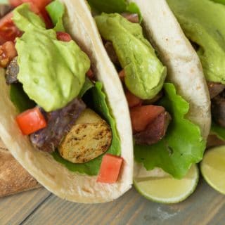 Three tacos filled with potatoes, peppers and a dollop of avocado sauce on top