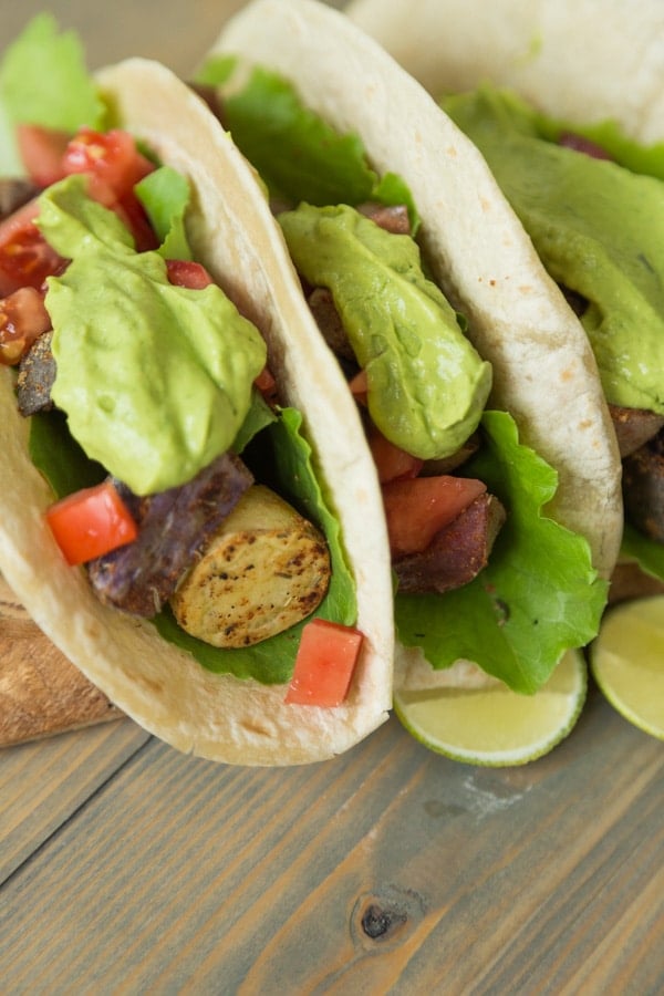 Three tacos filled with potatoes, peppers and a dollop of avocado sauce on top