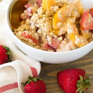 Strawberry Peach Overnight Oats in a white bowl with a gold spoon and strawberries on top of a wood board with a white and red napkin