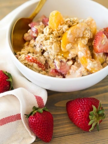 Strawberry Peach Overnight Oats in a white bowl with a gold spoon and strawberries on top of a wood board with a white and red napkin