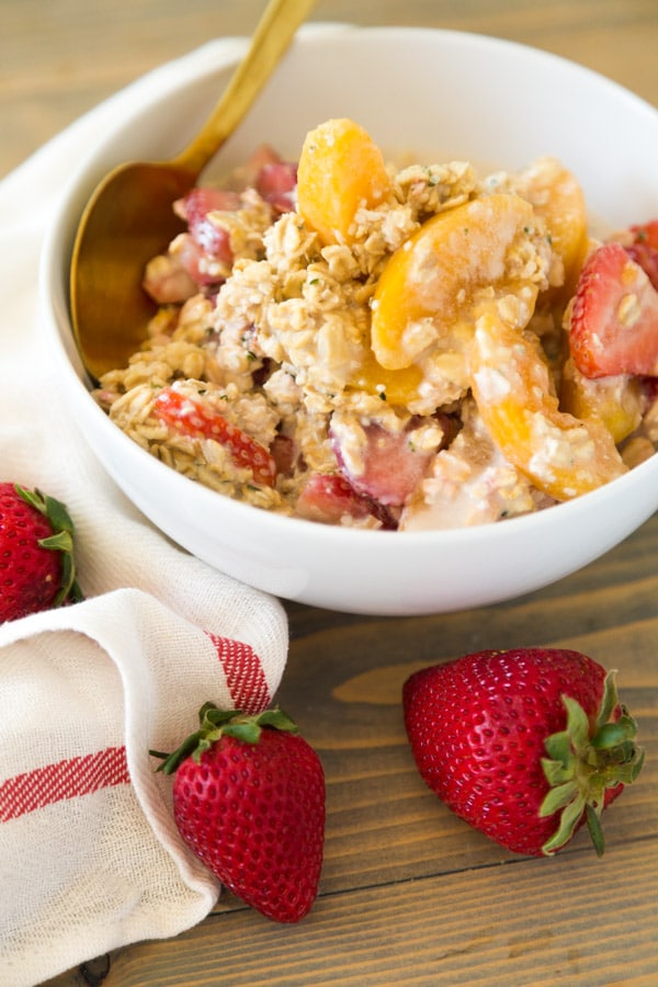 Strawberry Peach Overnight Oats in a white bowl with a gold spoon and strawberries on top of a wood board with a white and red napkin