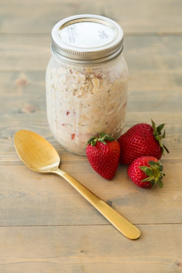 Strawberry Peach Overnight Oats in a mason jar with strawberries and a gold spoon next to it on top of a wood board