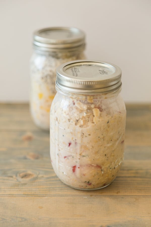 Strawberry Peach Overnight Oats in a mason jar with another jar of overnight oats behind it on top of a wood board