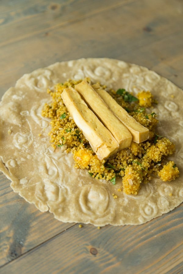 A tortilla on a wood board with curried quinao, mango and tofu about to be made into one of our curry tofu wraps