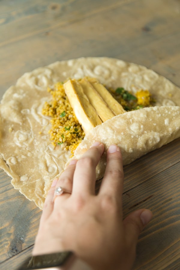 Folding the sides of a tortilla over one of our curry tofu wraps with quinoa, mango and tofu to make a wrap