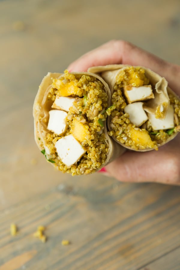 A hand holding a wrap with tofu and mango