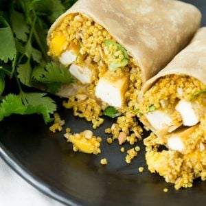 A wrap with tofu and quinoa on a black plate